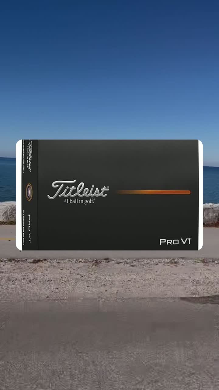 A dozen box of Titleist Pro V1 golf balls set against a calm lake and clear blue sky